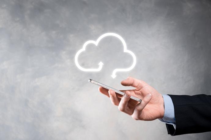 Cloud, lokale Lösungen, Clouddienste, Hand mit Handy darüber schwebt Wolke vor grauemn Hintergrund